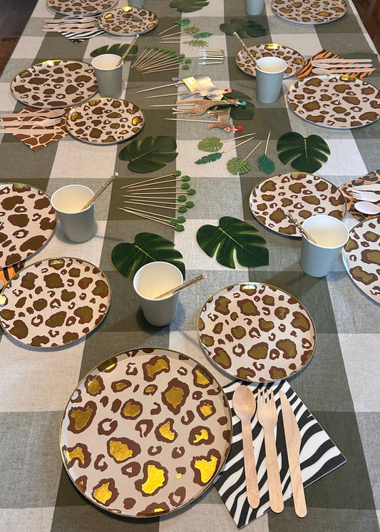 Table with leopard print plates, cups, and napkins on a checkered tablecloth.