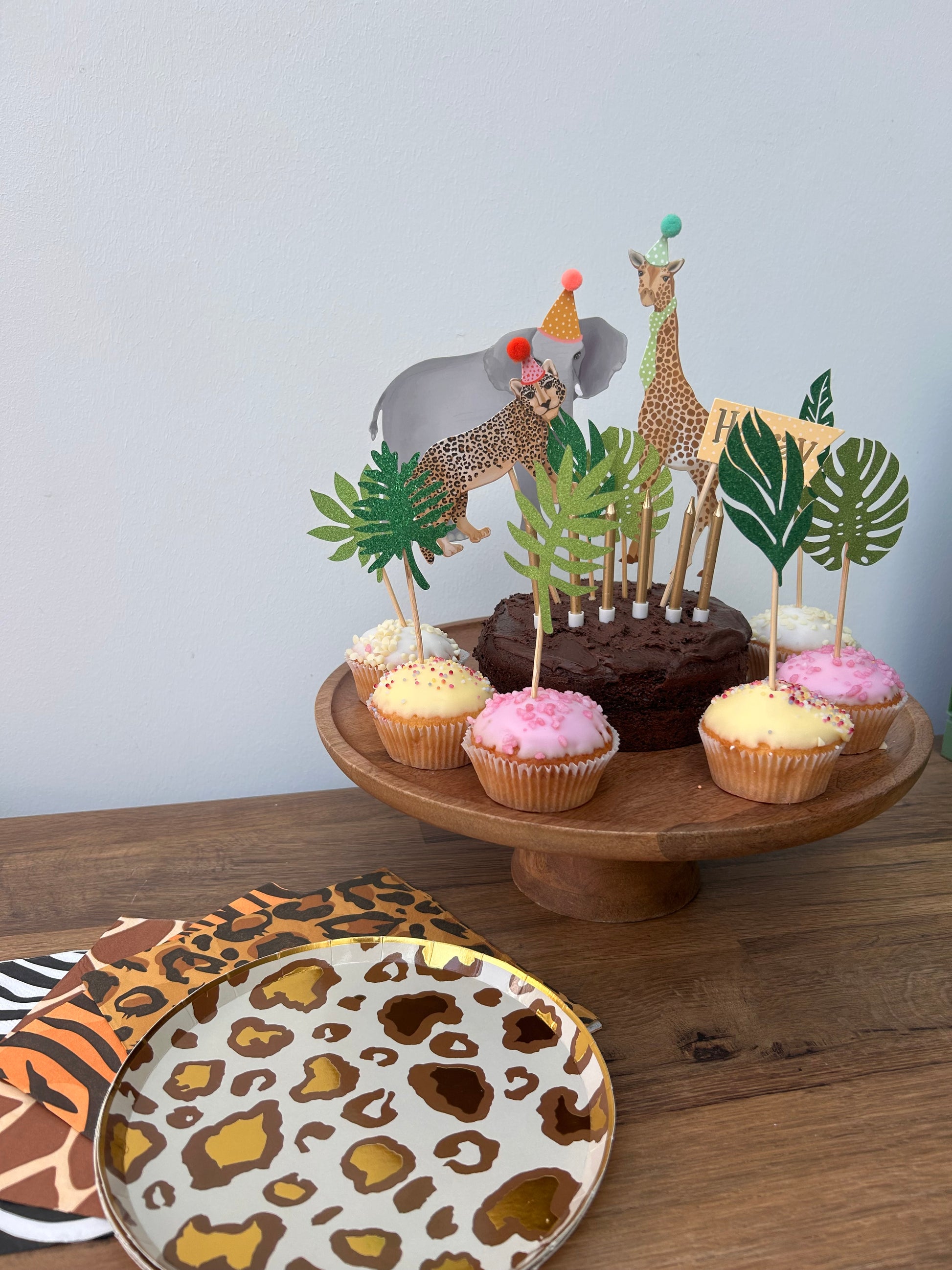 Decorative animal-themed dessert stand with cupcakes and a leopard print plate on a wooden surface.