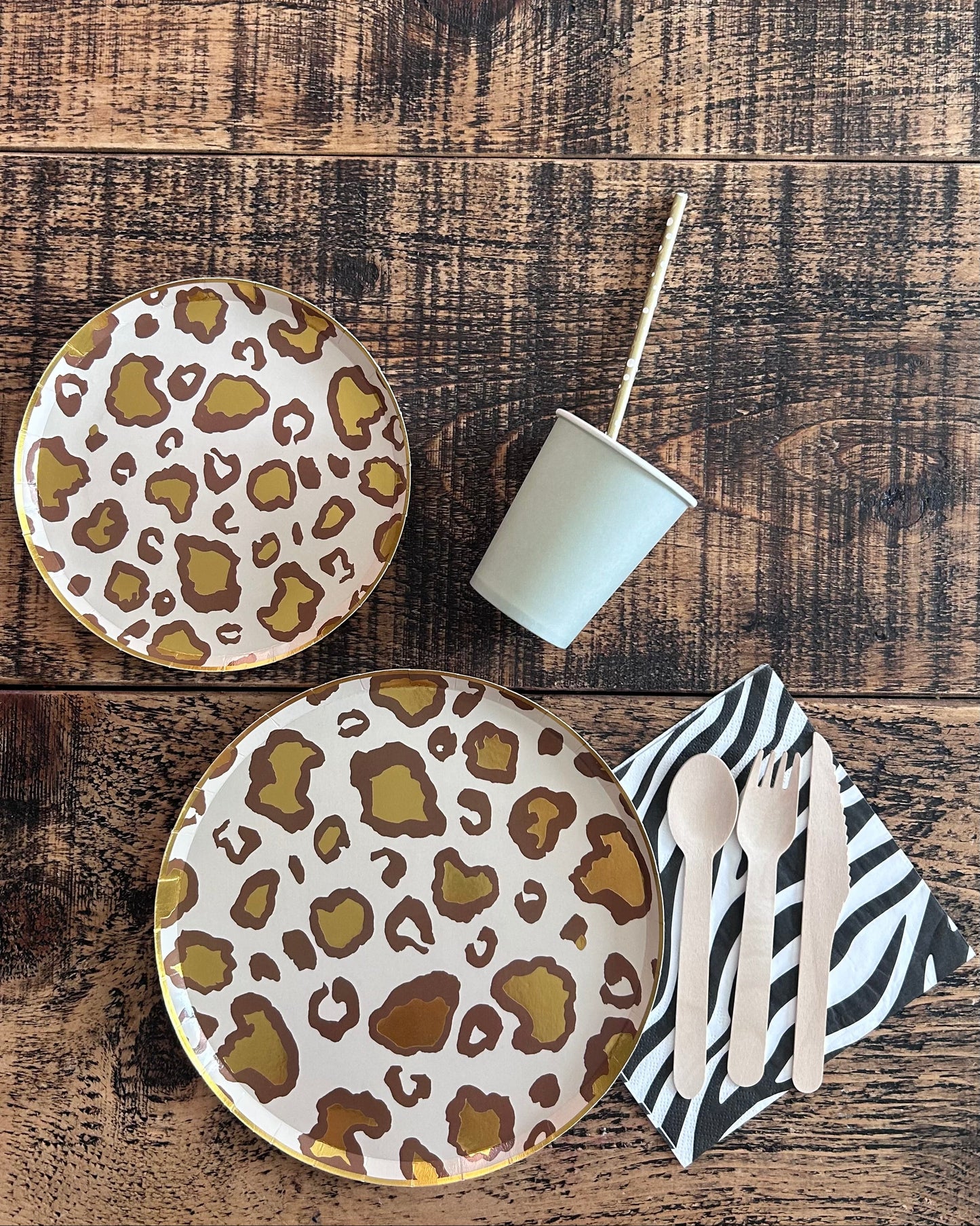 Two leopard print plates on a wooden surface with cutlery and a napkin.