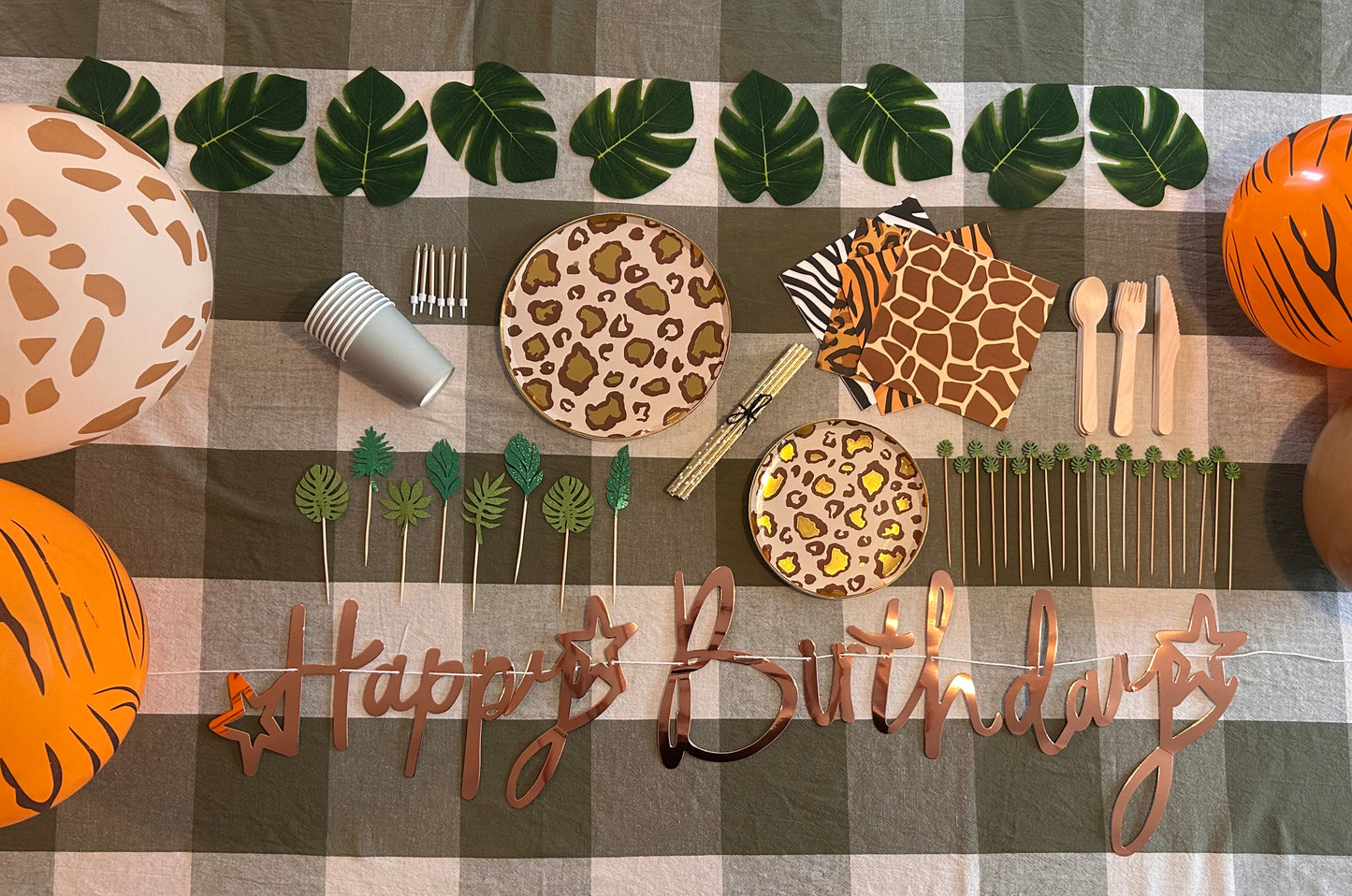 Birthday table setup with animal print plates, cutlery, and 'Happy Birthday' sign on a checkered tablecloth.