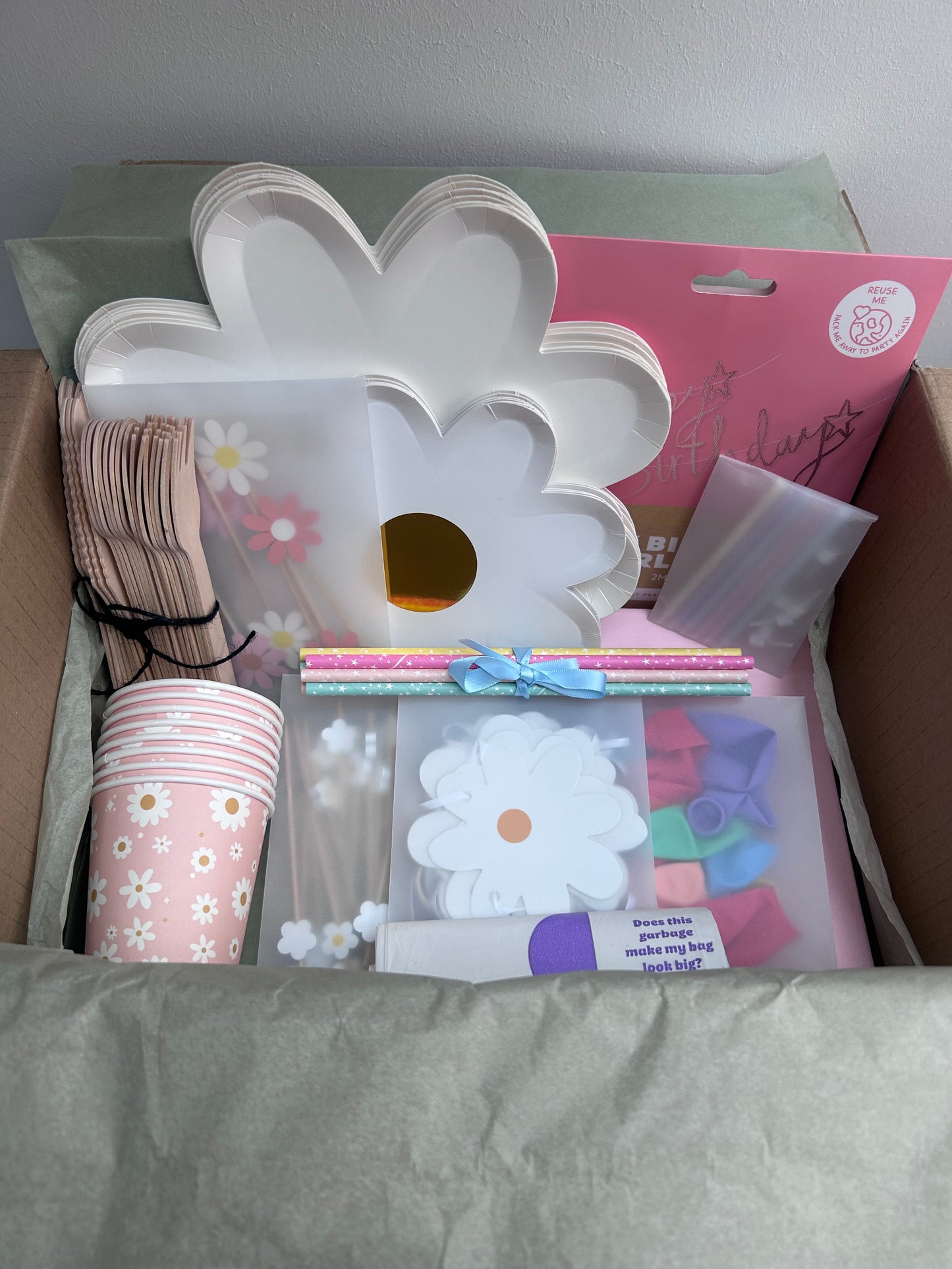 Assorted party supplies including a white flower-shaped cake stand, pink cups with floral designs, and other decorative items on a gray surface.