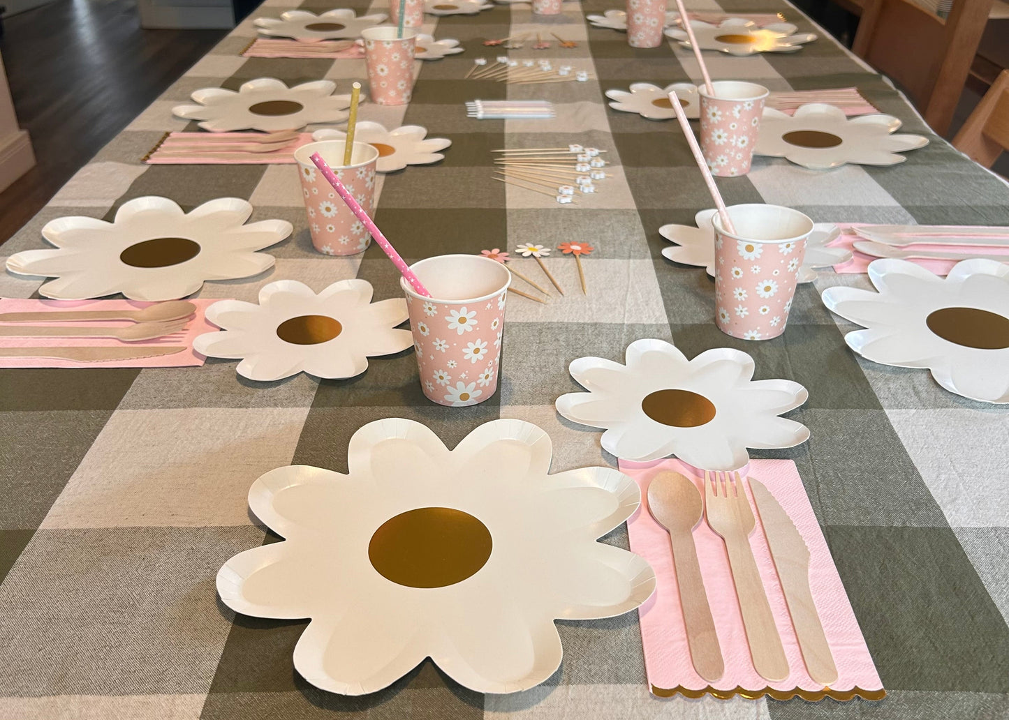 Table setting with flower-shaped plates, cups, and cutlery on a checkered tablecloth.