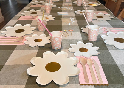 Table setting with flower-shaped plates, cups, and cutlery on a checkered tablecloth.
